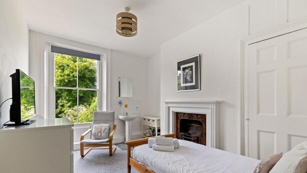 A bedroom with a bed, a chair, a desk, a fireplace, and a window with a view of greenery. - Dover Town Rooms (Dover)