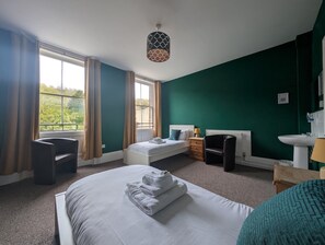 A hotel room with a bed, a chair, a desk, a radiator, and a window with curtains. - Dover Town Rooms (Dover)