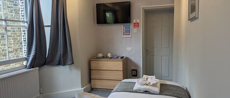 Una habitación de hotel con cama, cómoda, televisor montado en la pared, ventana con cortinas y puerta.