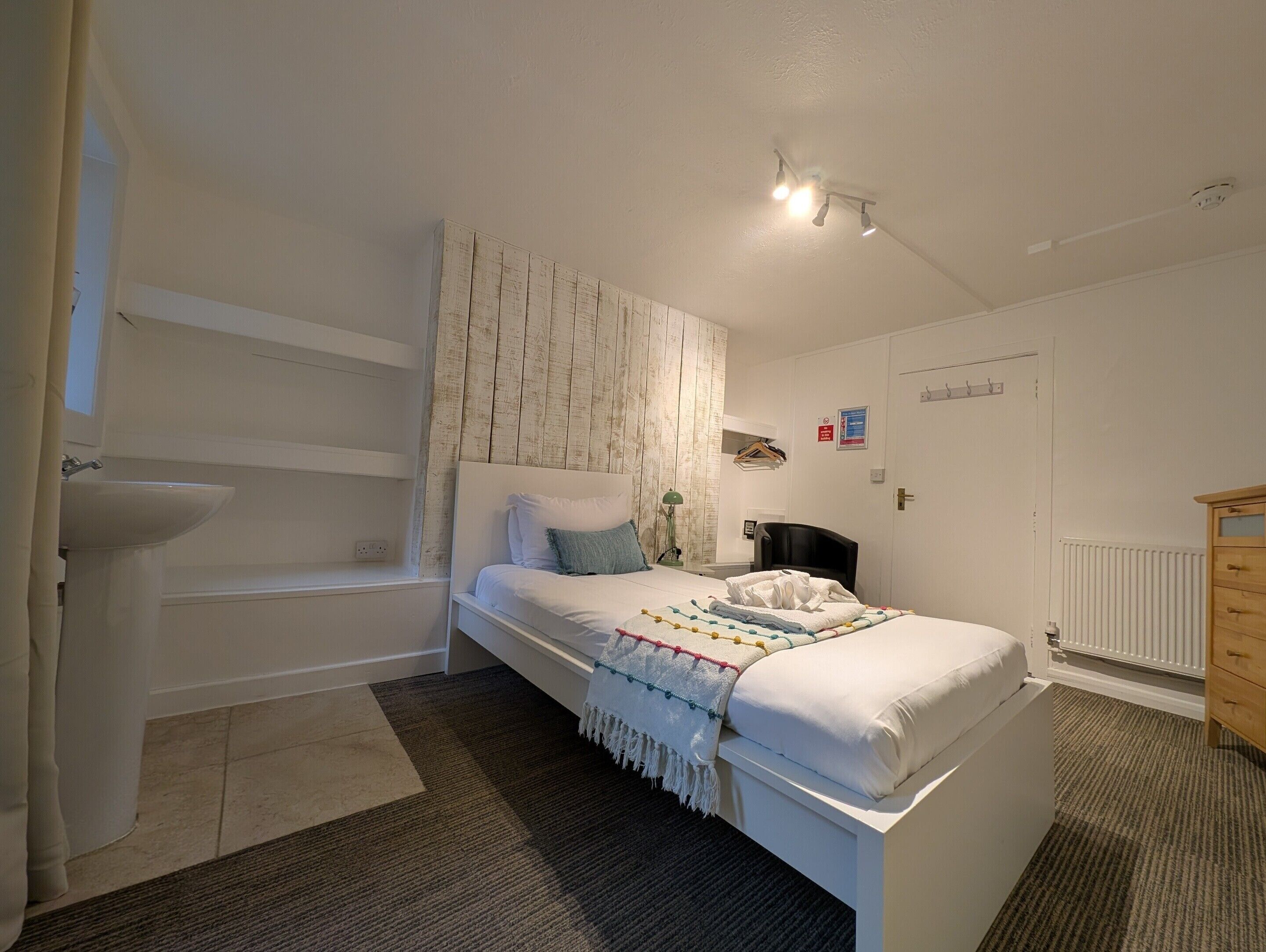 Ein Schlafzimmer mit Bett, Nachttisch, Pendelleuchte, Heizkörper und Tür.