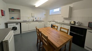 A compact kitchen with a washing machine, a stove, a sink, and a dining table with chairs. - Dover Town Rooms (Dover)