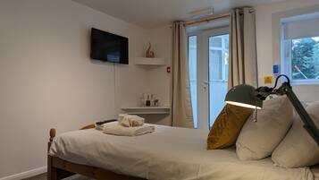 A bedroom with a bed, a television mounted on the wall, a bedside table with a lamp, and a window with curtains.
