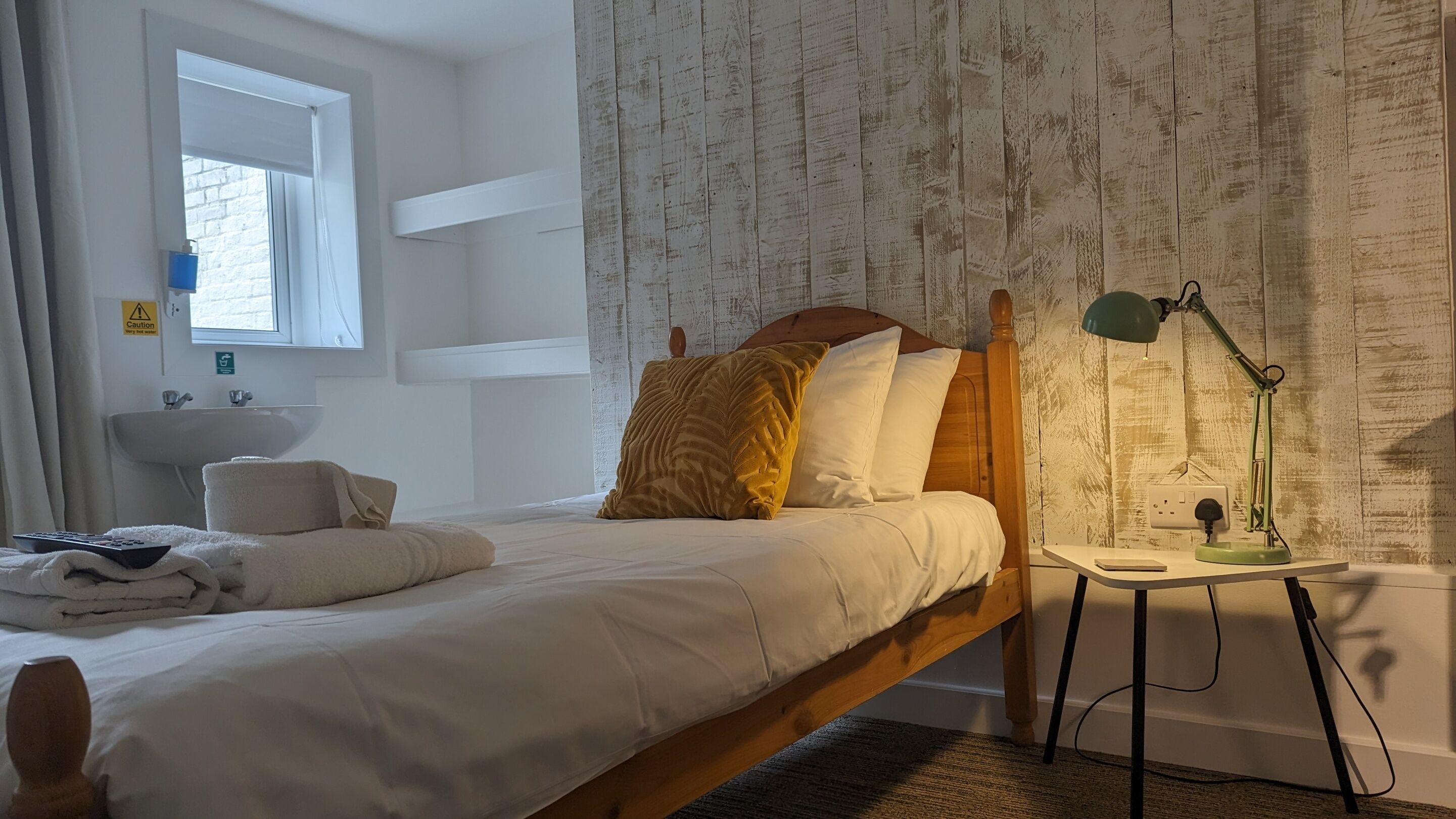 Ein Schlafzimmer mit einem Bett, einem Nachttisch mit Lampe, einem Fenster und einem Badezimmer mit Waschbecken.