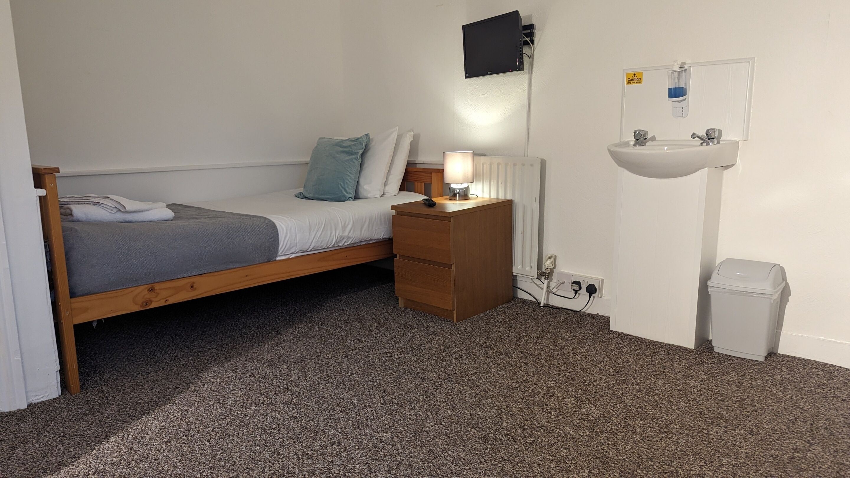 Un dormitorio pequeño y ordenado con una cama individual, mesita de noche con lámpara y lavamanos integrado.