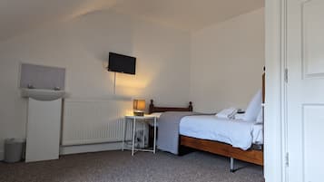A bedroom with a bed, a bedside table, a TV mounted on the wall, and a radiator.