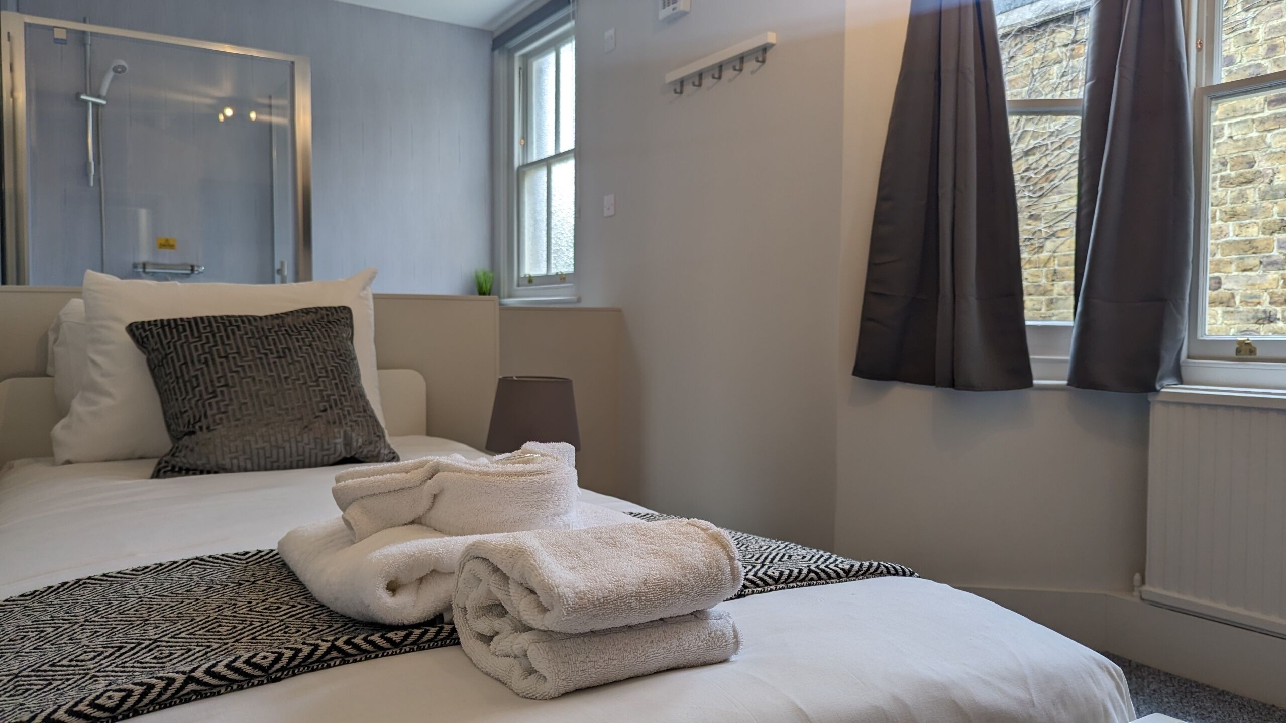 A hotel room with a bed, a shower, a window with curtains, and a radiator.