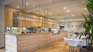 A modern bar area with wooden cabinetry, a glass display case, and white chairs. - West Court - Cambridge - Campus Accommodation (Cambridge)