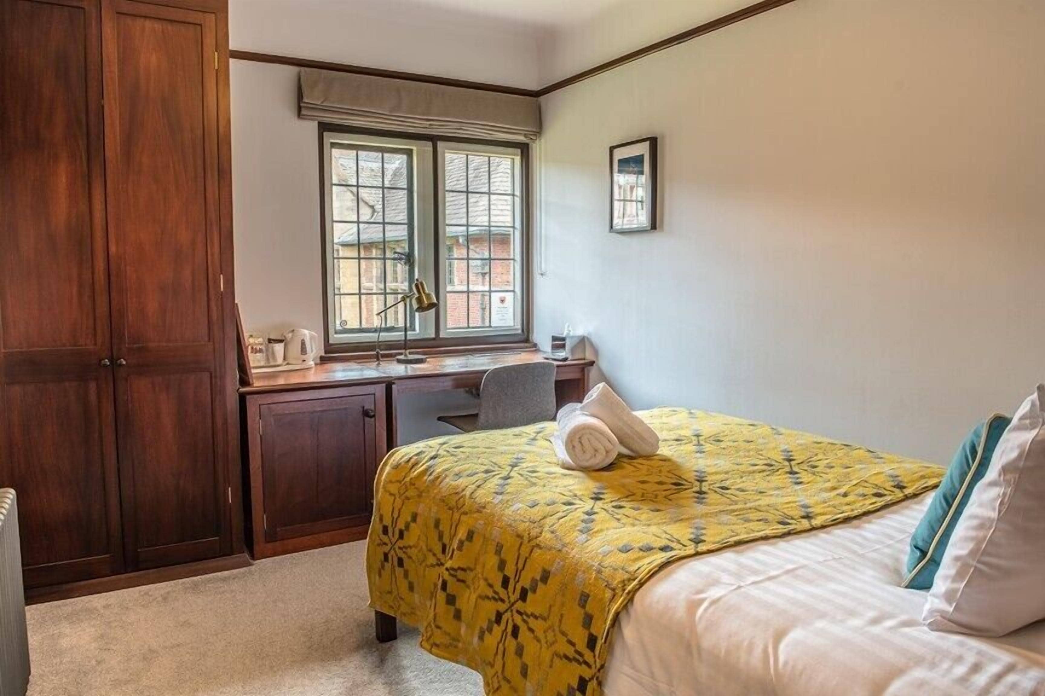 A bedroom with a bed, a desk, and a window.