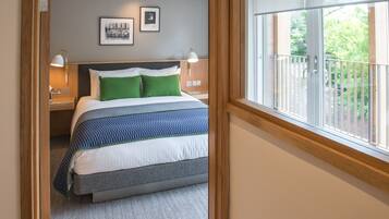 A bedroom with a bed, two bedside lamps, a window with a view of greenery, and a framed picture on the wall.