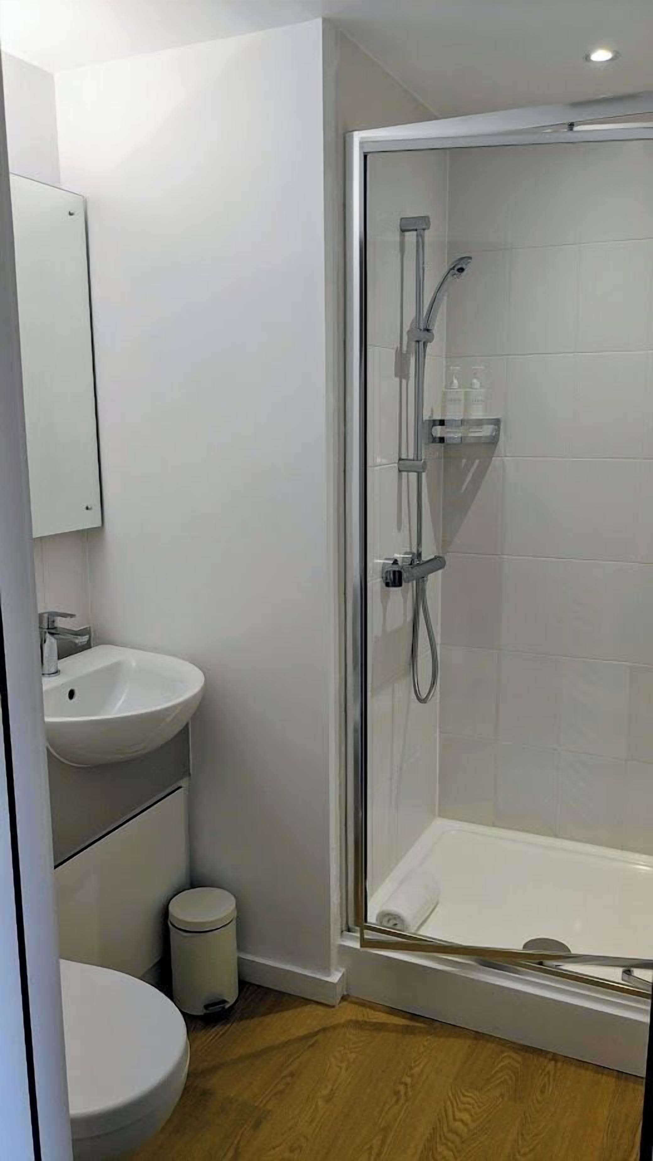 A modern bathroom with a glass-enclosed shower, a white sink, and a toilet.
