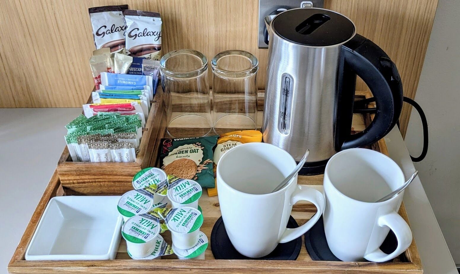 A tray with coffee cups, milk cartons, a kettle, and various breakfast items.
