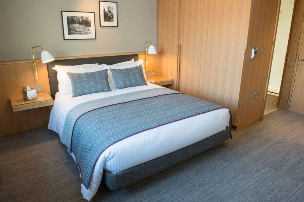 A neatly made bed with a blue and white duvet, two bedside lamps, and a wooden wardrobe in a hotel room.