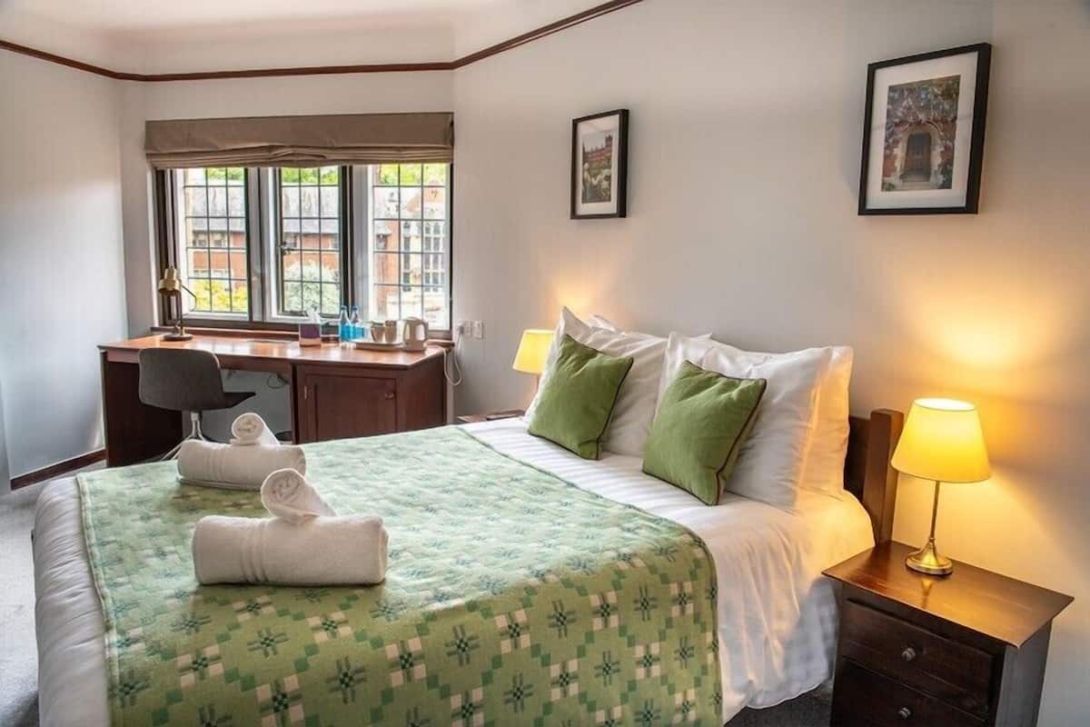 A hotel room with a bed, a desk, and a chair. There are two lamps on the nightstand.
