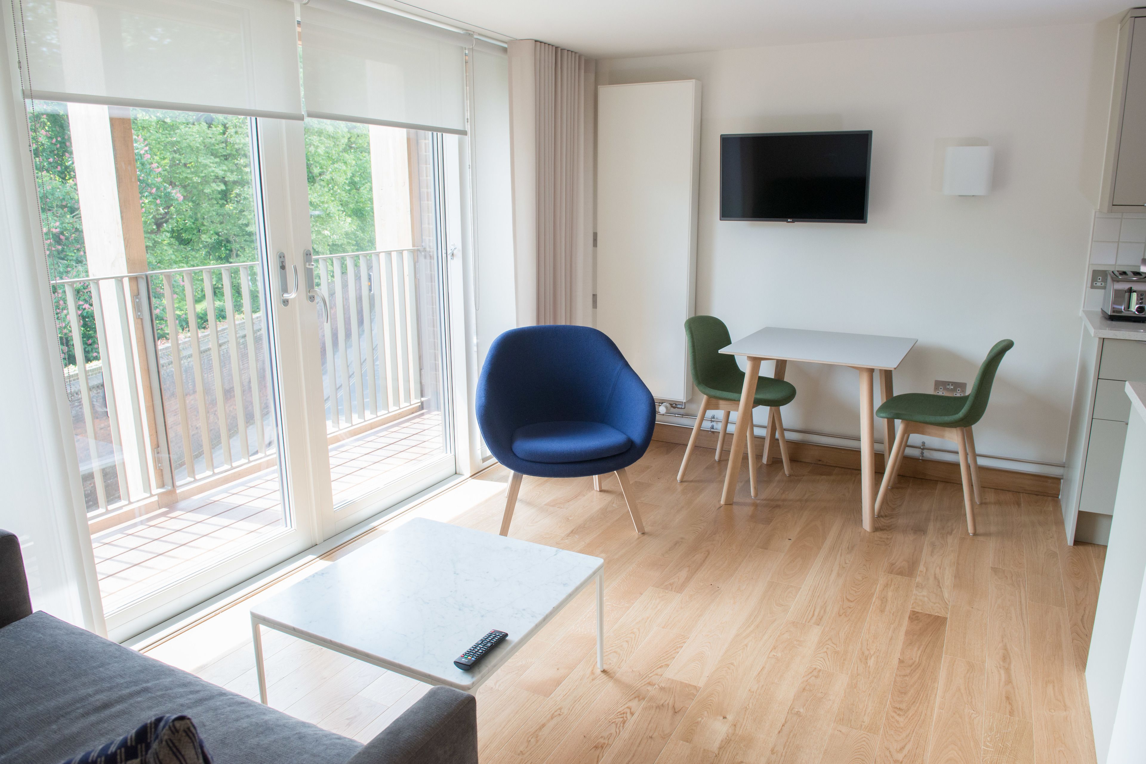 A modern living room with a balcony, a dining area, and a TV mounted on the wall.