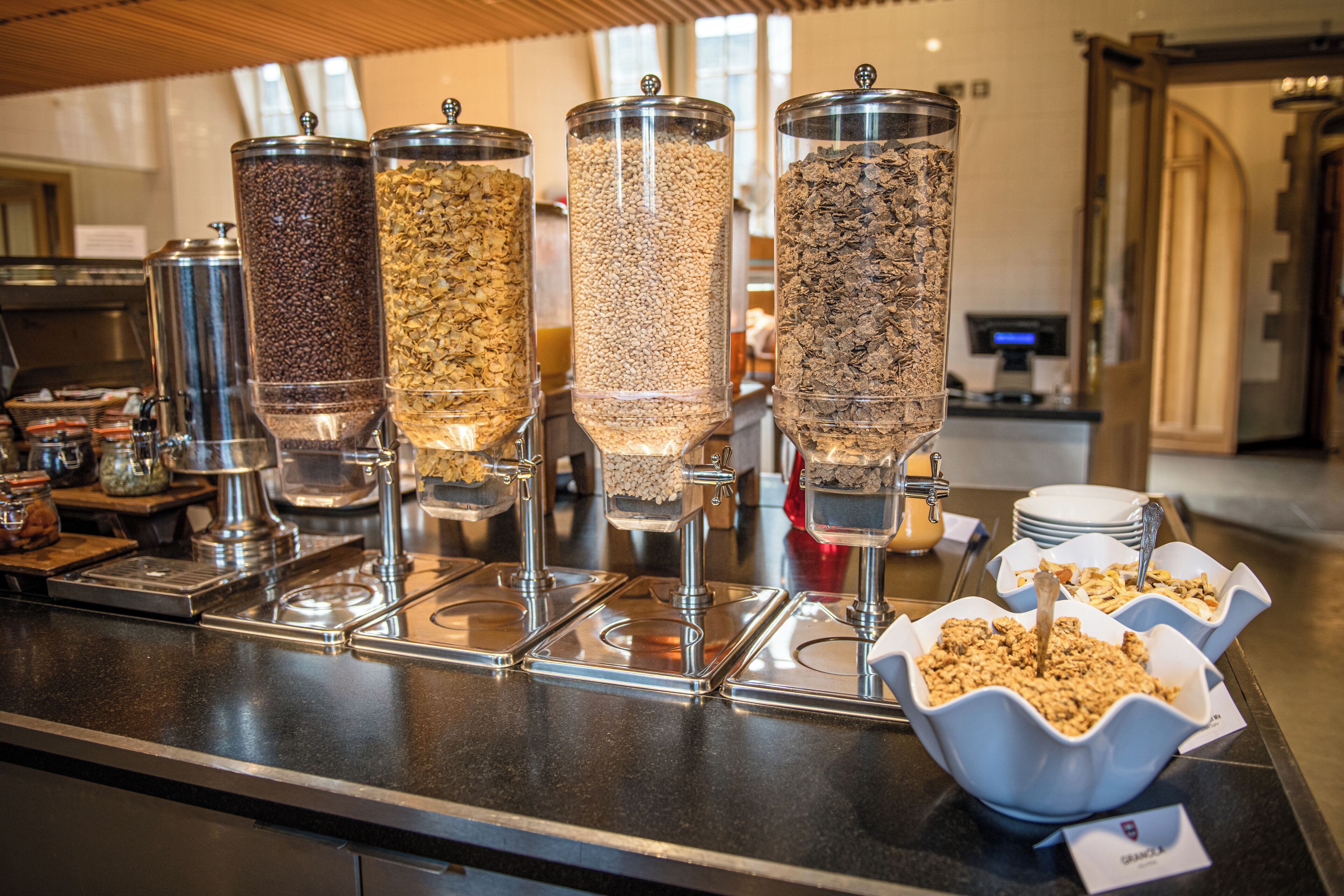 A buffet with various food dispensers and bowls of cereal.