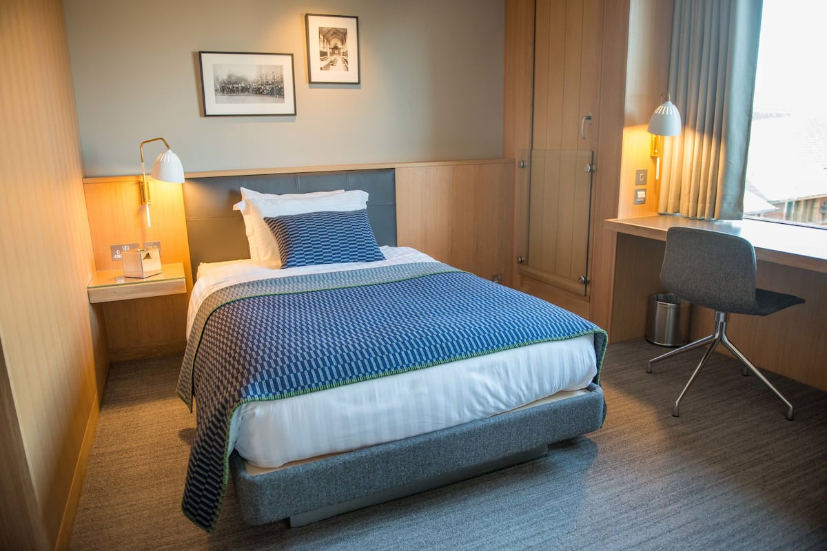 A hotel room with a bed, bedside tables, a desk, and a chair.