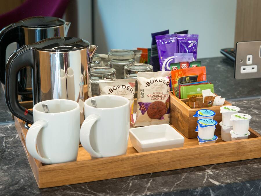 Una bandeja con tazas de café, un hervidor, frascos y aperitivos envasados.