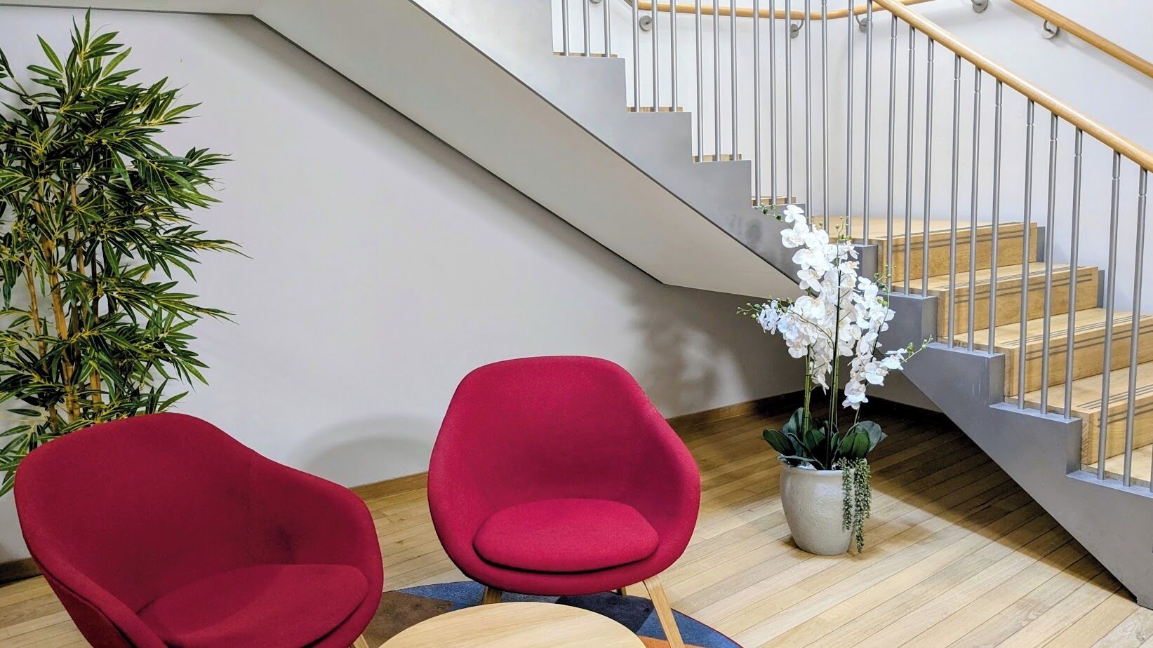 Interior moderno com escada, duas cadeiras vermelhas, uma pequena mesa e um vaso de planta.
