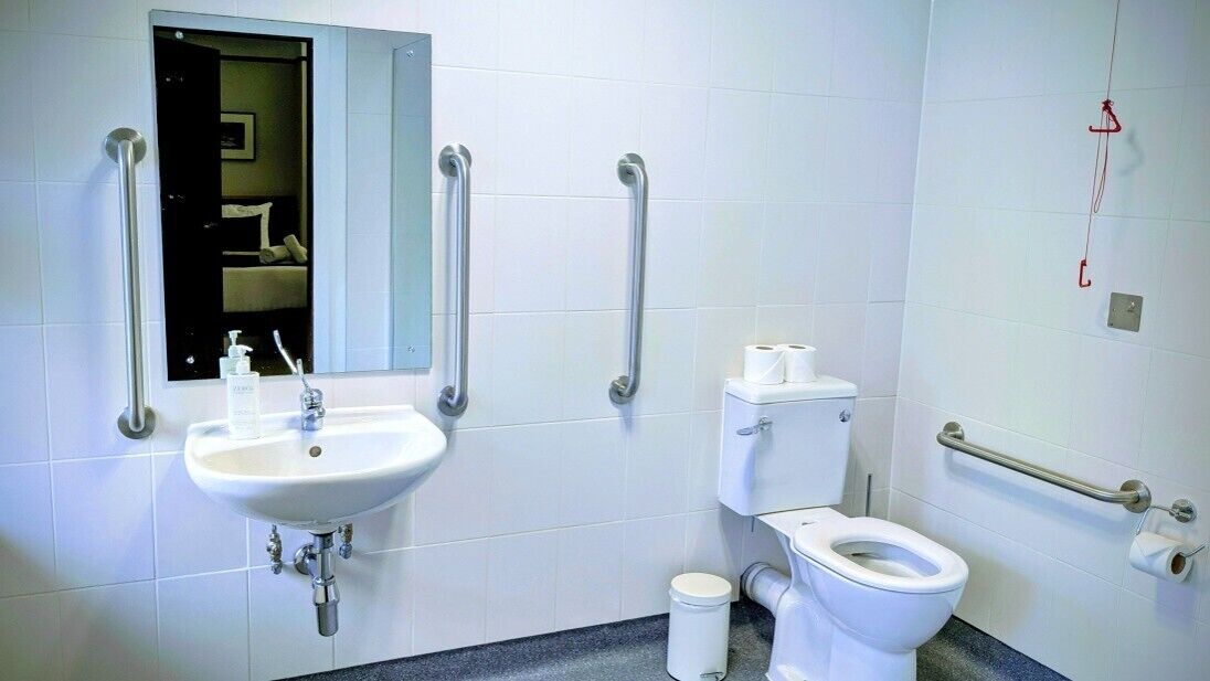A bathroom with a sink, mirror, toilet, and grab bars.