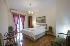 A hotel room with a large bed, two chairs, a painting on the wall, and a window with curtains. - Keramikos Cozy Apartment (Athens)