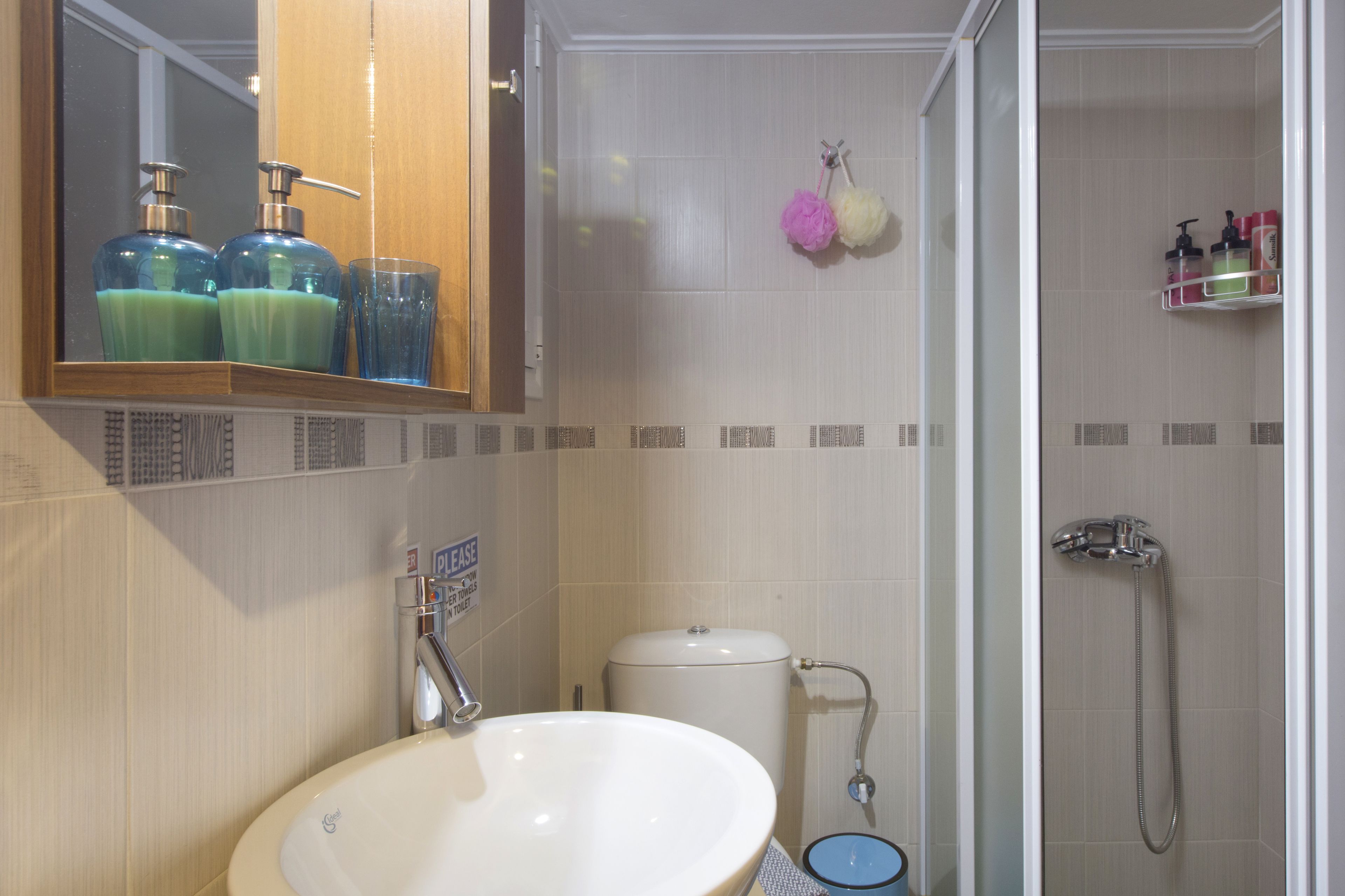 A bathroom with a sink, toilet, and shower. There are soap dispensers and a hanging showerhead.
