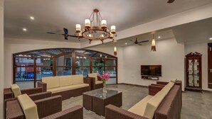A spacious living area with wicker furniture, a glass coffee table, a chandelier, a ceiling fan, and a large window offering a view of the outside. - 10 Bedroom Private Pool Villa in Calangute with Jacuzzi, Kids Pool, Mini Golf (Calangute)