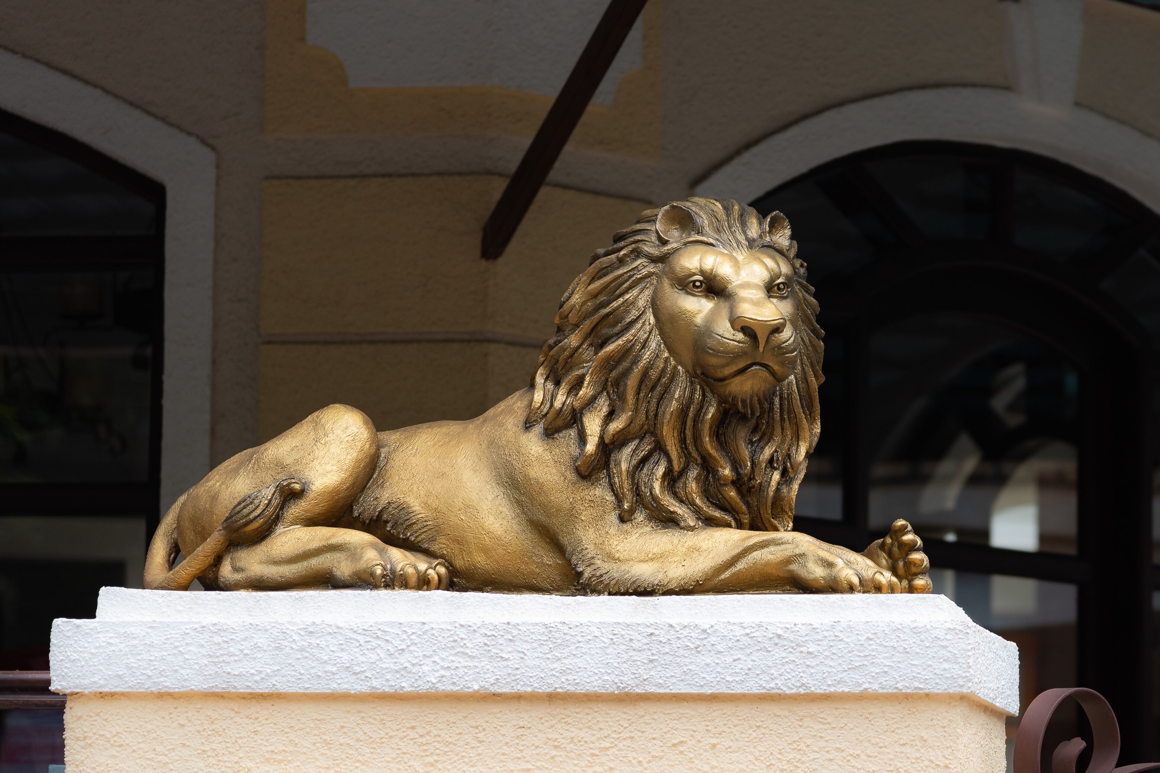 Una estatua dorada de león sobre un pedestal blanco.