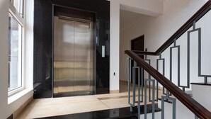 A modern elevator with a metallic finish, a wooden staircase with metal railings, and a light-colored floor. - 10 Bedroom Private Pool Villa in Calangute with Jacuzzi, Kids Pool, Mini Golf (Calangute)