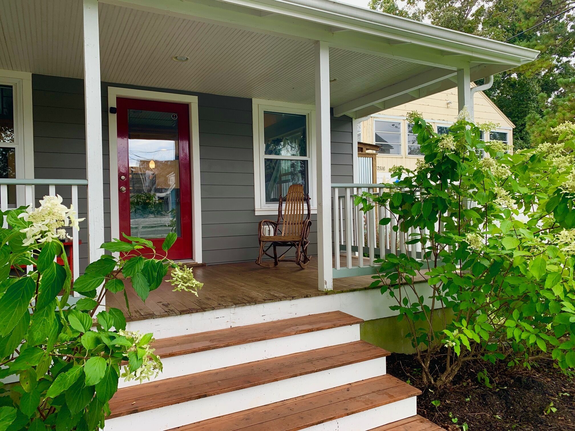 A porch with a red door, a rocking chair, and steps leading to a house.