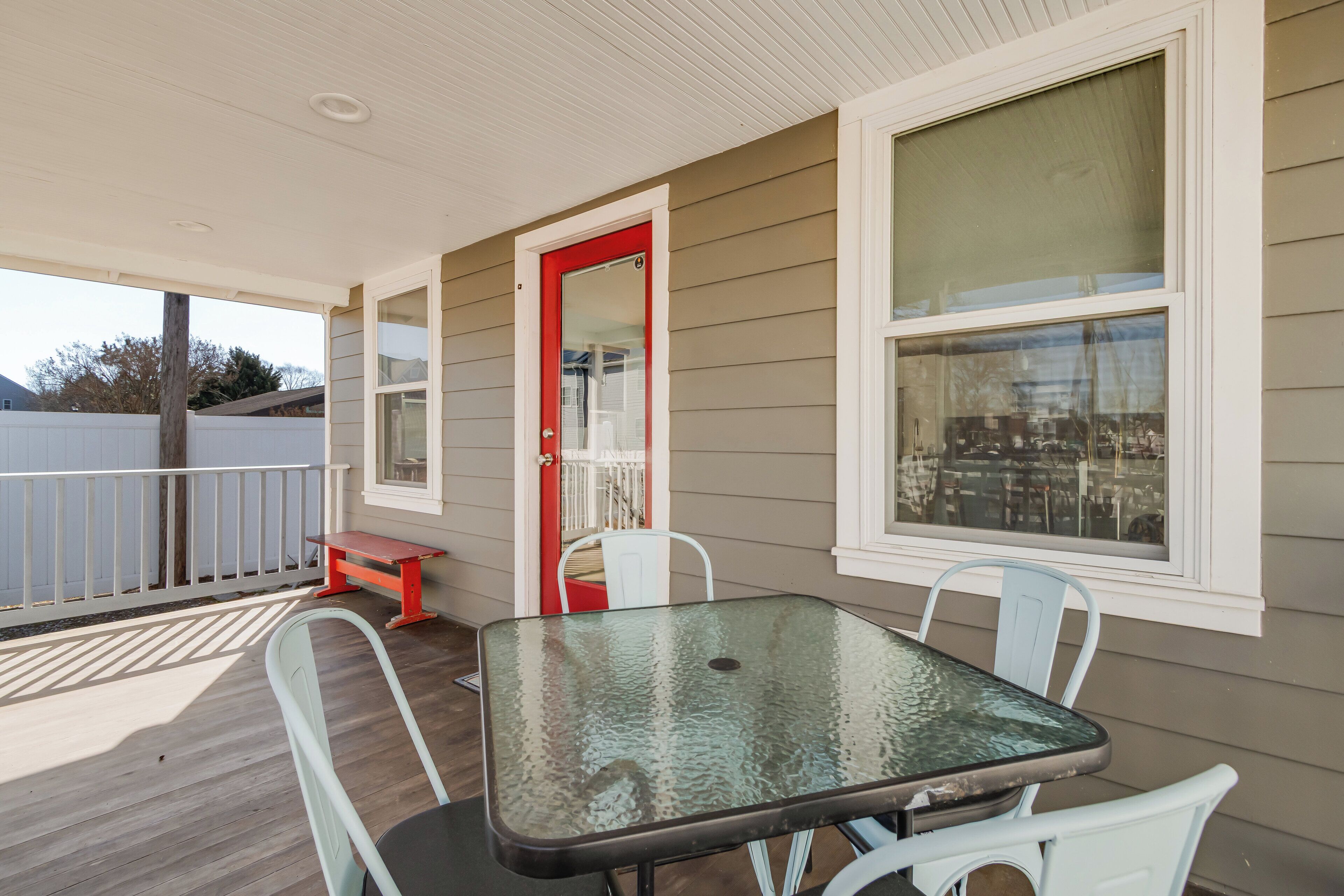 A covered porch with a glass table and white chairs, a red door, and a view of the neighborhood.