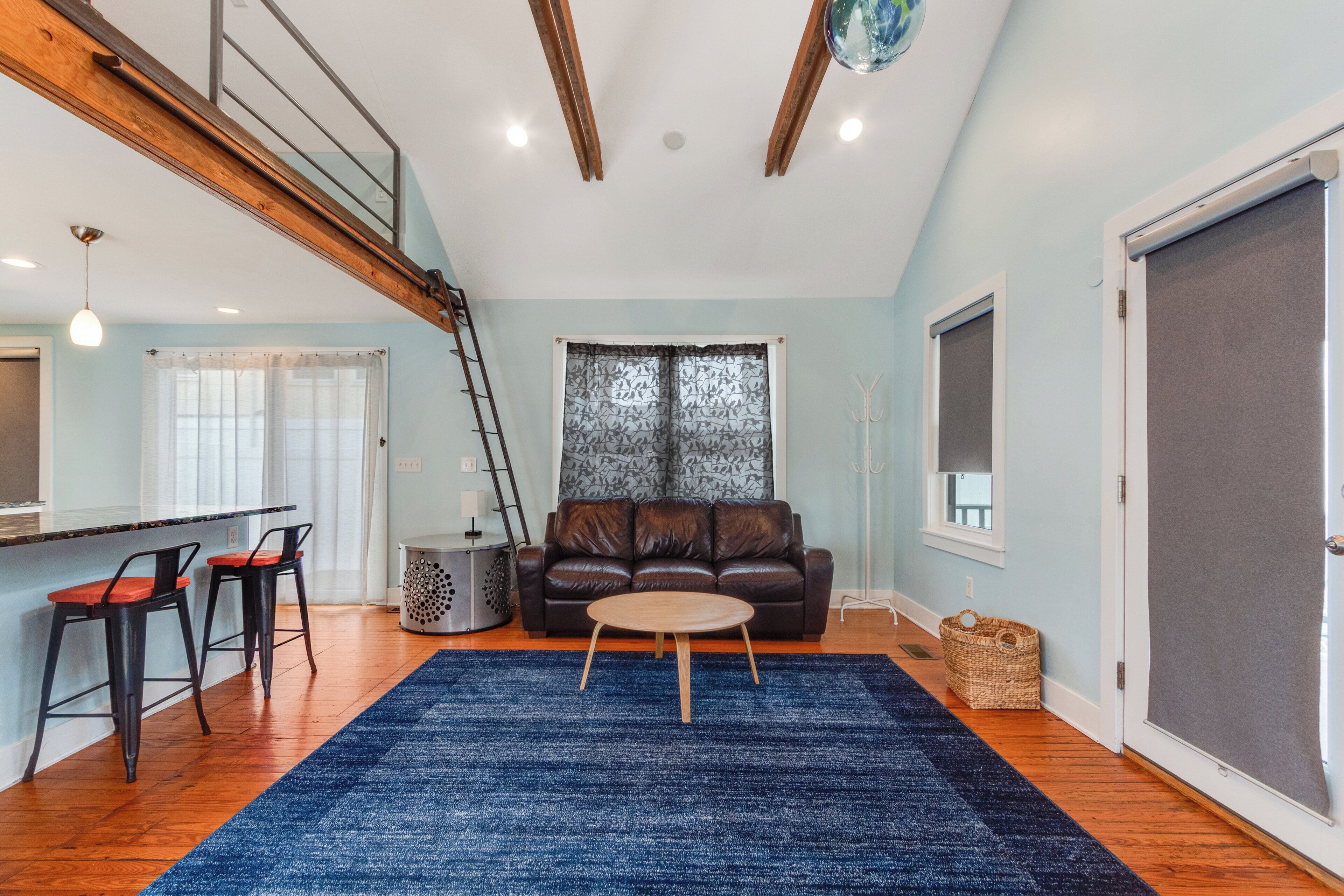 A living room with a blue rug, a brown leather sofa, and a wooden coffee table.