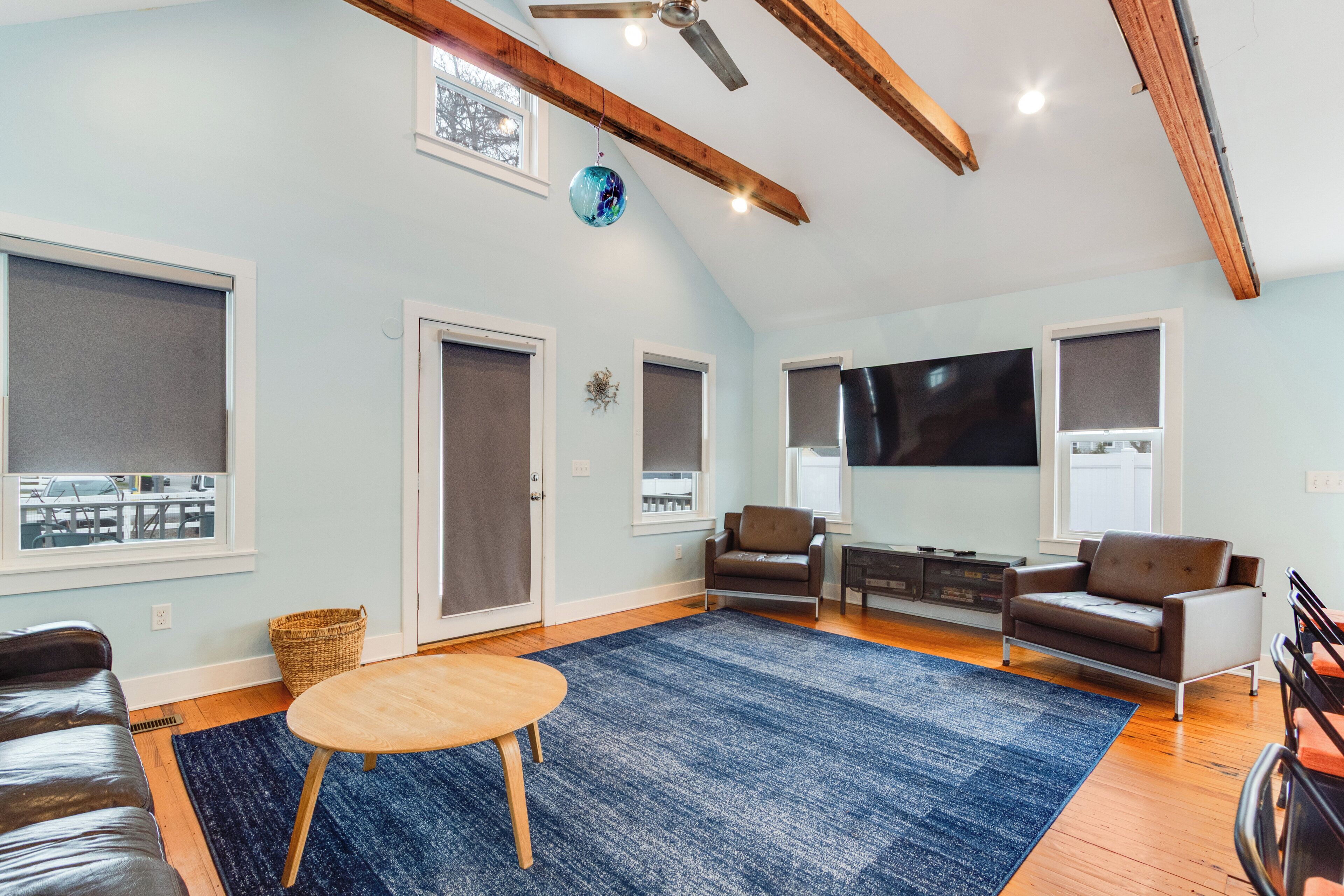Un salón amplio con televisor grande, vigas de madera en el techo y alfombra azul.