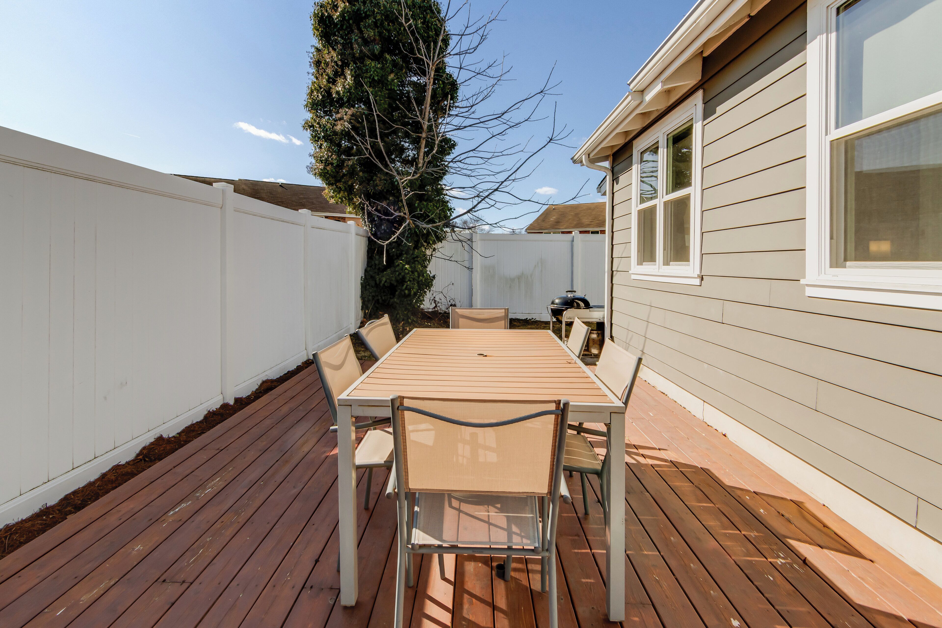 A wooden deck with a table and chairs, a white fence, and a house with windows.