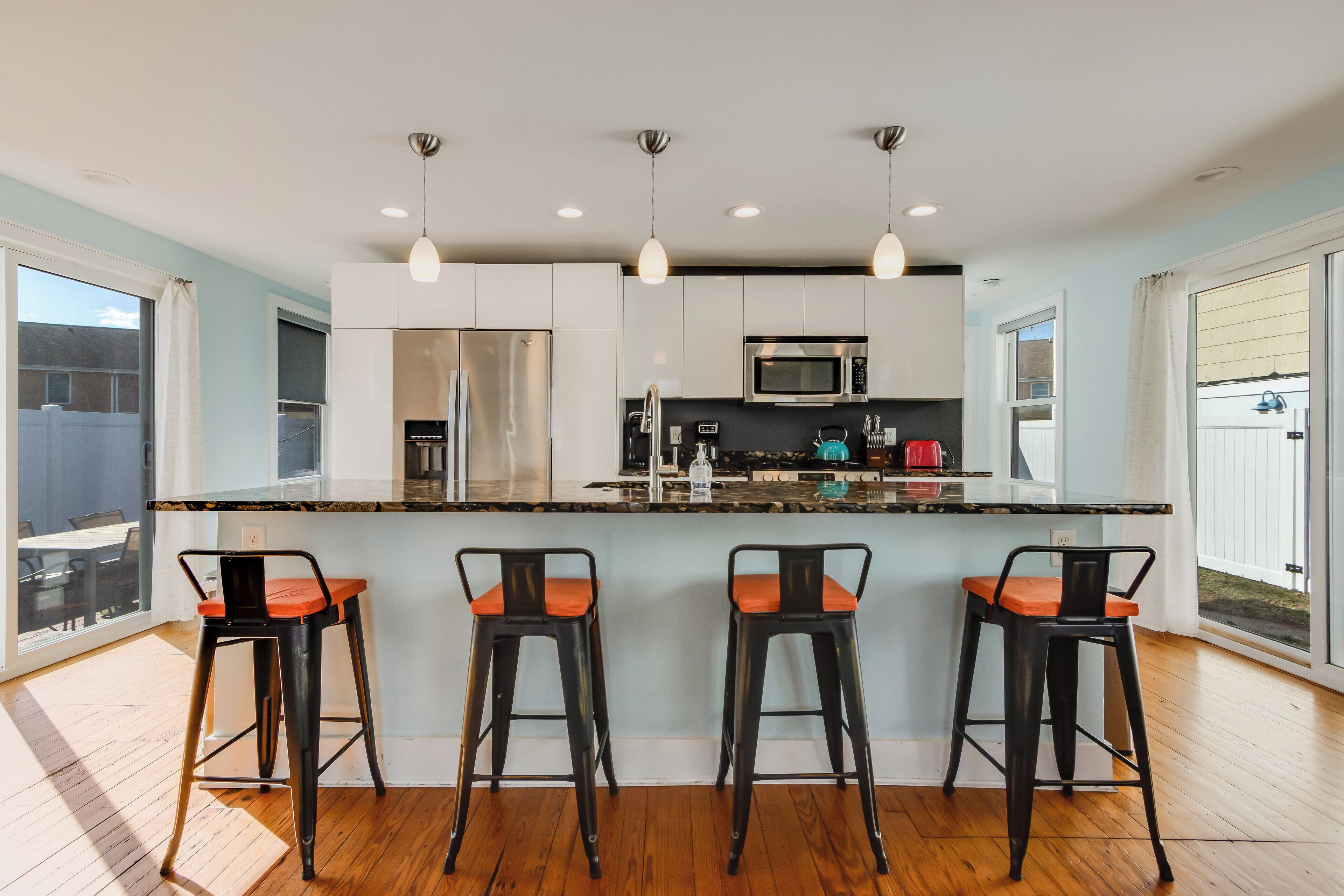 A modern kitchen with a central island, bar stools, stainless steel appliances, and pendant lighting.