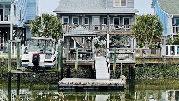 Una casa frente al agua con un muelle, un bote y un porche con escaleras.