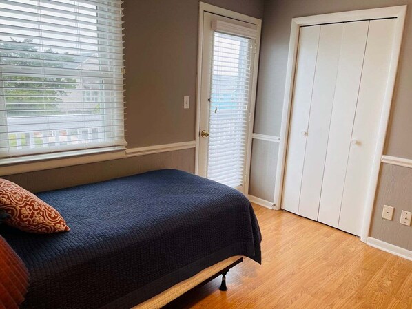 A bedroom with a bed, a window with blinds, a door, and a wardrobe. - Beach Bells – Cozy 4-BR home in Holden Beach with easy beach access. (Holden Beach)