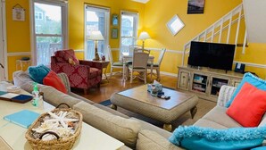 Una sala de estar con paredes amarillas, un sofá, un sillón rojo, un televisor y un comedor con una mesa y sillas.