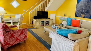 Una sala de estar con escalera, televisor, mesa de comedor y sofá.