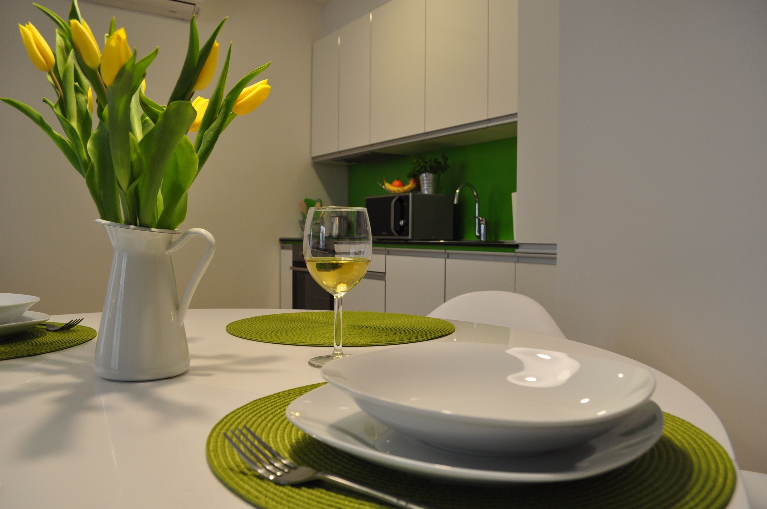 Een eettafel met witte borden, een glas witte wijn en een vaas gele tulpen.