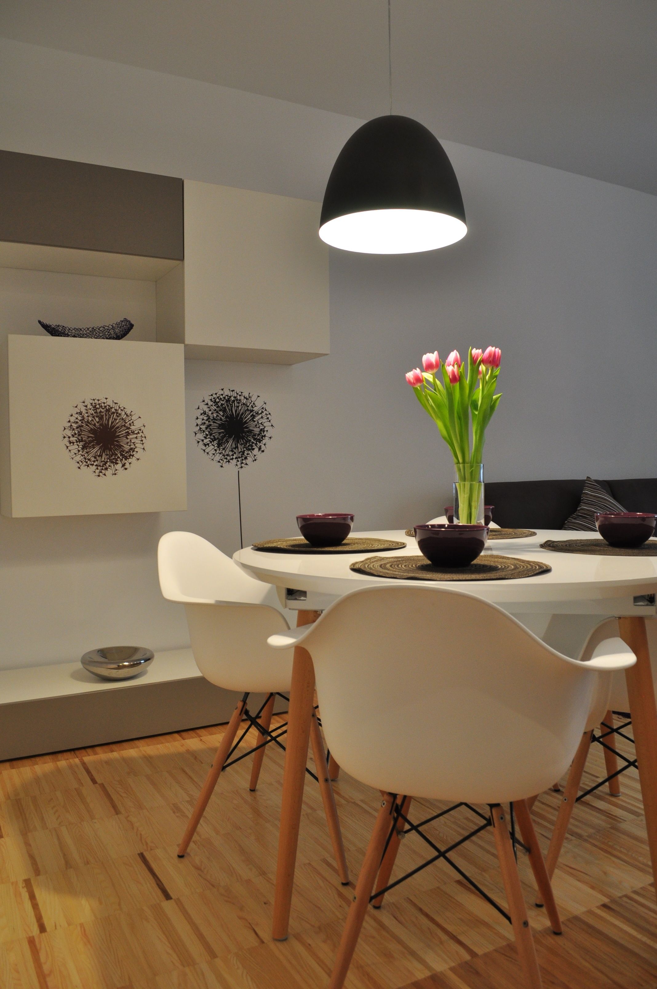 Een moderne eethoek met een witte tafel, een zwarte hanglamp en witte stoelen.