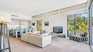 A spacious living room with a large TV, a sofa, and a dining area with chairs. - Luxury condo, ocean views, sea breeze, pool, tennis court, minutes to cafes (Sapphire Beach)