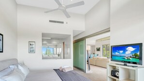 A modern bedroom with a bed, a ceiling fan, a TV, and a large mirror. - Luxury condo, ocean views, sea breeze, pool, tennis court, minutes to cafes (Sapphire Beach)