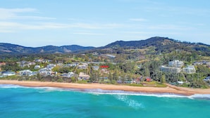 A coastal town with beachfront properties, a mountain backdrop, and a clear sky. - Luxury condo, ocean views, sea breeze, pool, tennis court, minutes to cafes (Sapphire Beach)