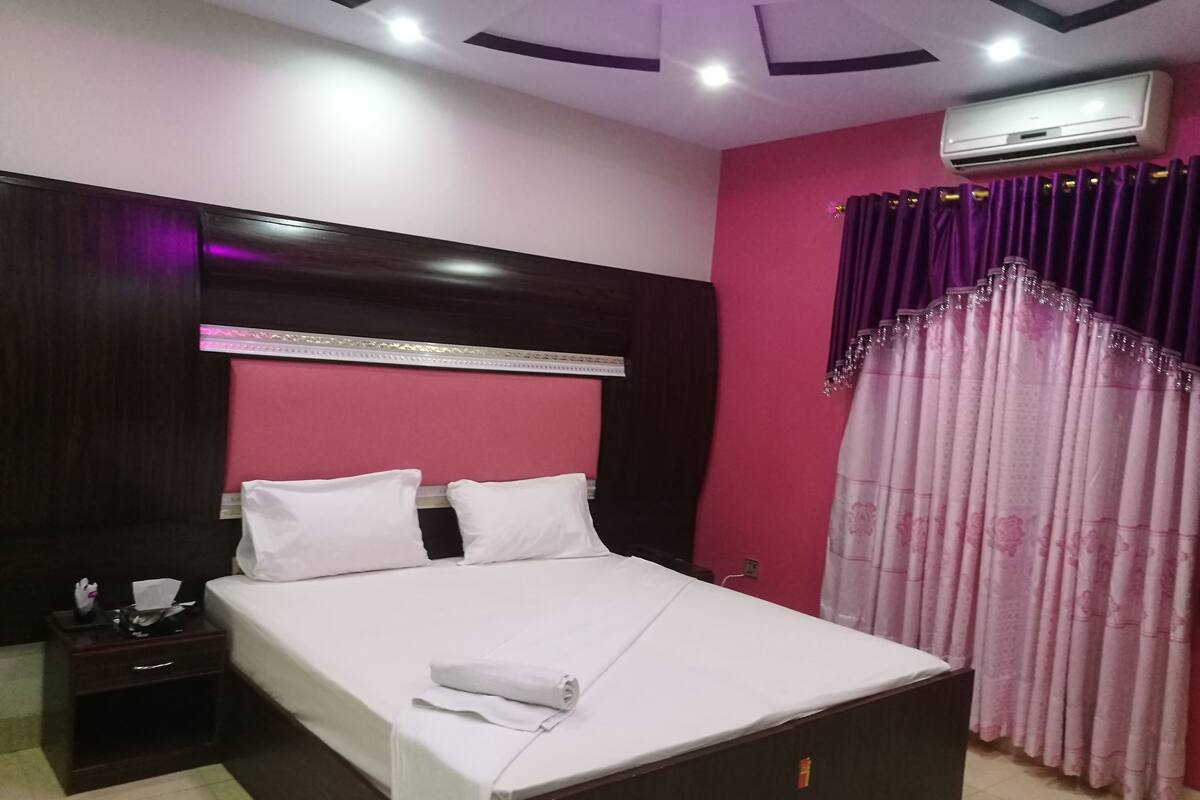 Una habitación de hotel con cama, mesita de noche y unidad de aire acondicionado.