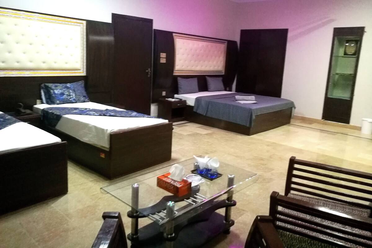 Habitación de hotel con dos camas, una mesita de vidrio, una silla y un ventilador de techo.
