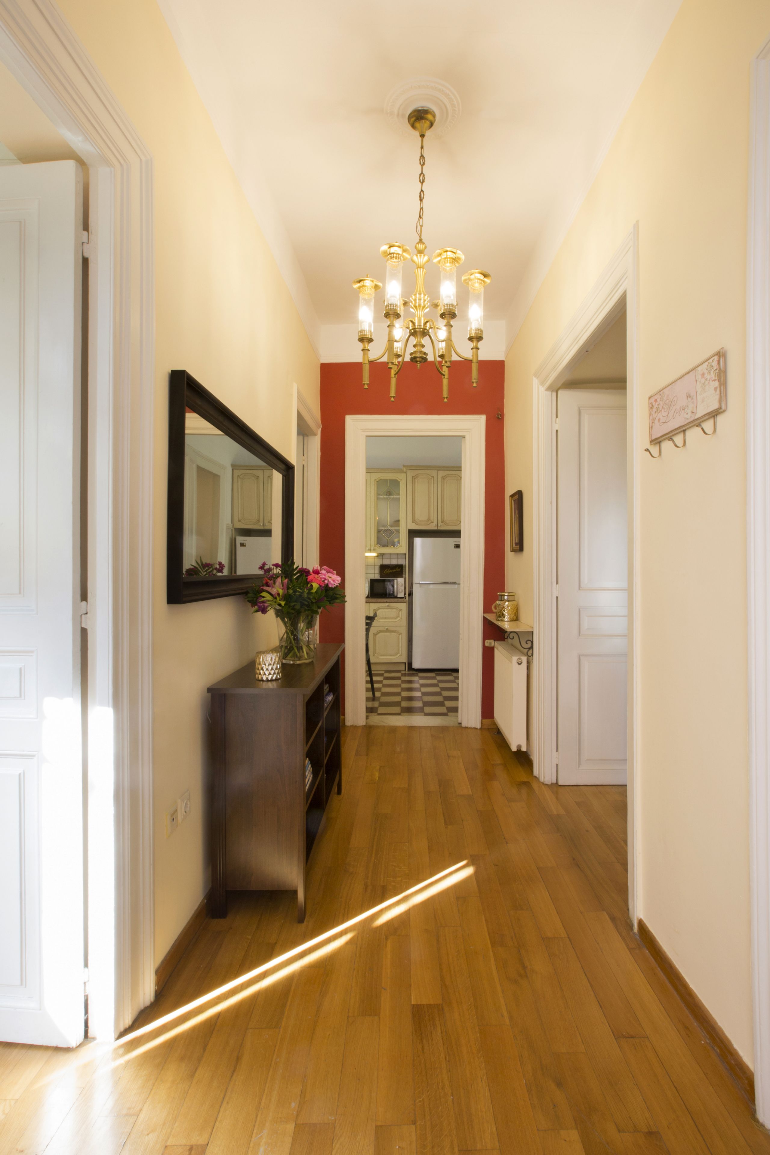 A hallway with wooden flooring, a chandelier, a mirror, and a vase with flowers.