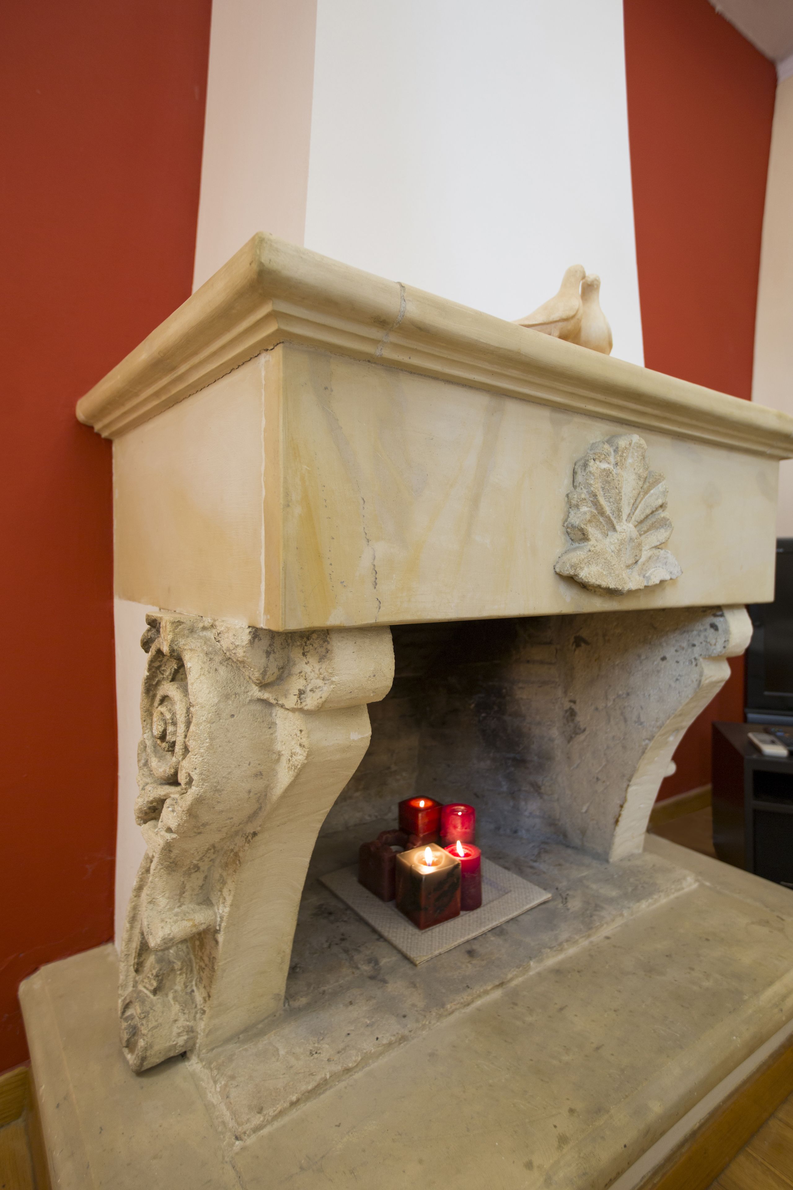 A stone fireplace with a carved leaf design, a small bird sculpture, and three lit candles on a mantel.