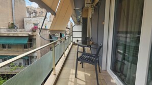 A balcony with a table and chairs, a railing, and a view of neighboring buildings. - Homely Stay at Acropolis Museum (Athens)