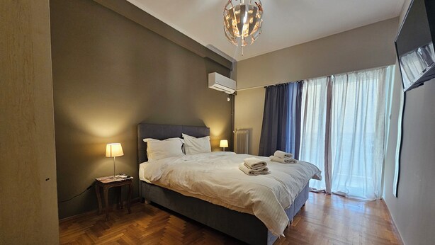 A bedroom with a large bed, two bedside lamps, a ceiling light fixture, and a window with curtains. - Homely Stay at Acropolis Museum (Athens)
