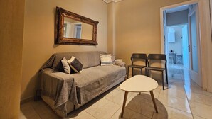 A living room with a sofa, a coffee table, a mirror, and a door leading to another room. - Homely Stay at Acropolis Museum (Athens)